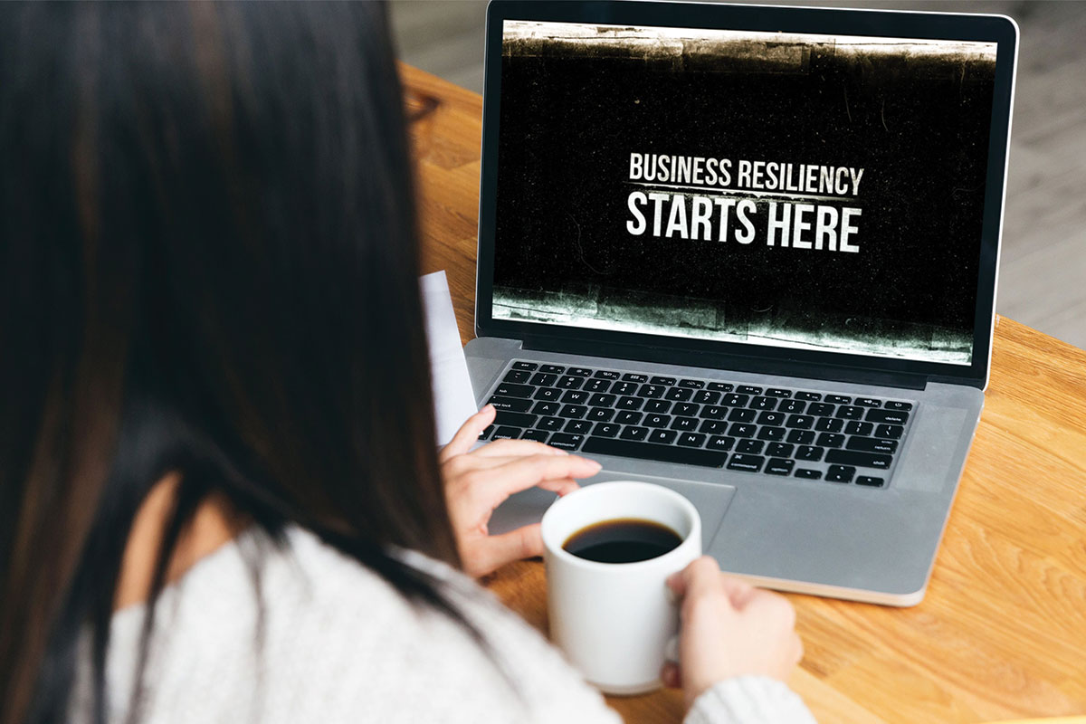 Lady with laptop and coffee. Laptop screen says Business Resiliency Starts Here.