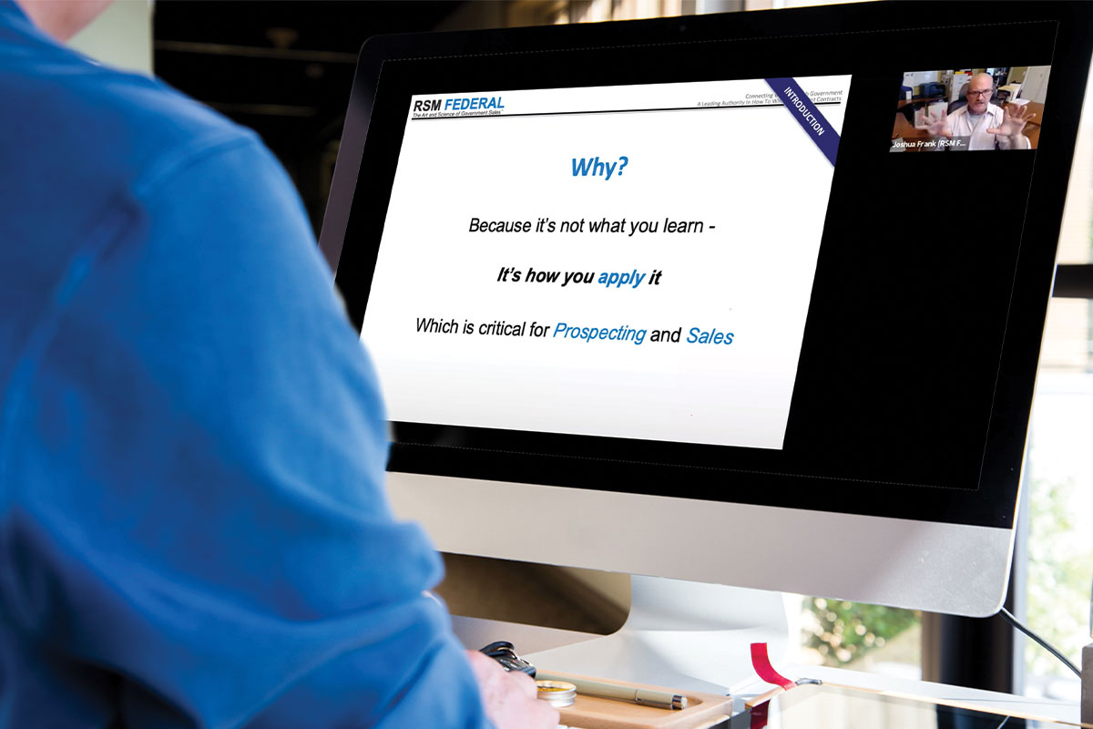 Person in blue shirt at desk watching a live webinar on computer.