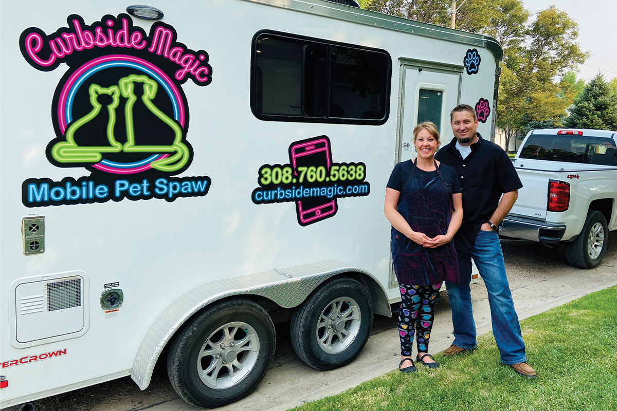 Owner, Dodi Megli of Curbside Magic Mobile Pet Spa standing with dog in front of trailer.
