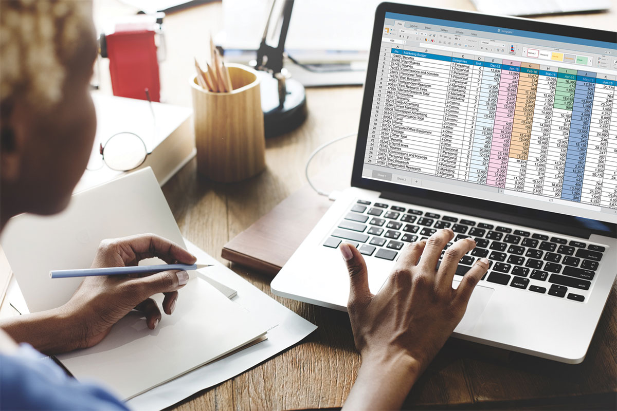 Female's hands working at laptop with spreadsheet displayed.