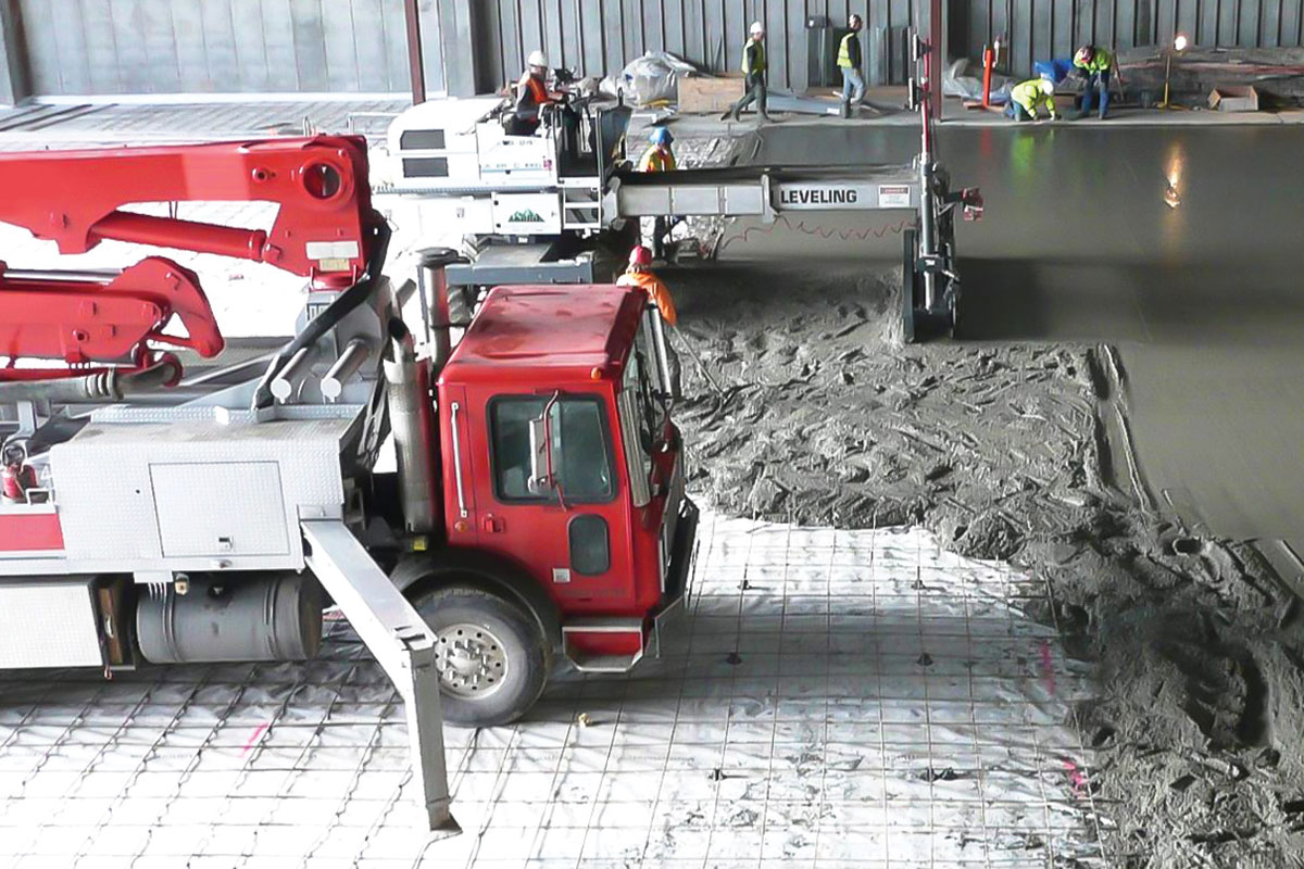 Fuller Construction: workers pouring concrete flooring in large building with leveling machinery.