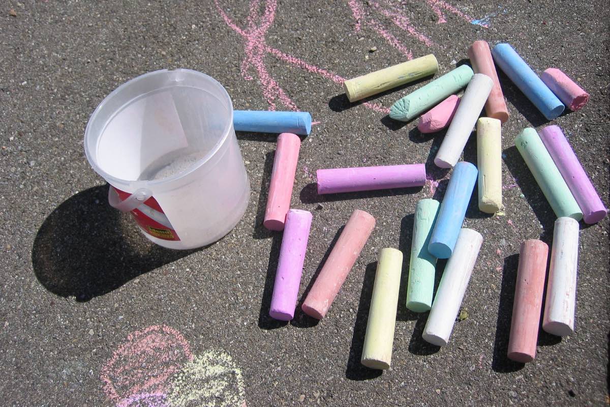 spilled bucket of chalk with children's drawing on pavement.