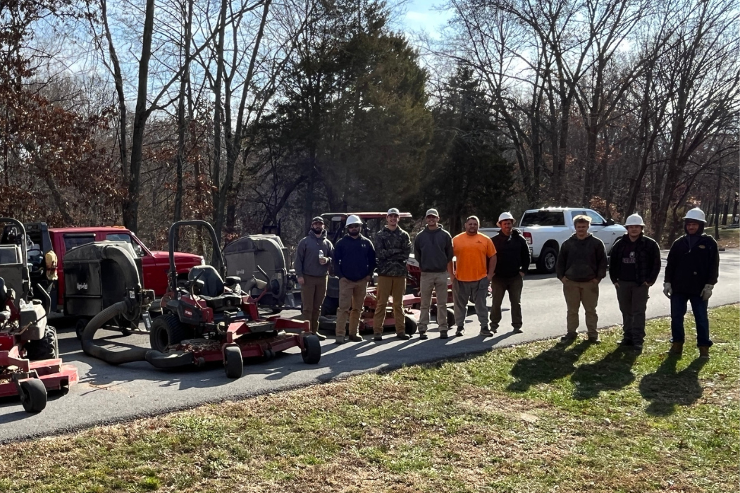 Group of construction workers with pieces of lawn equipment outdoors at a job site.