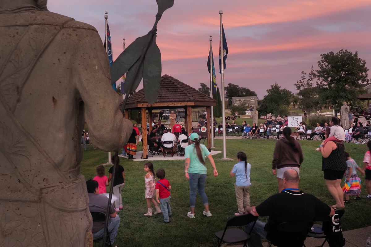 Group of people in a park at sunset. Musicians sit in a gazebo. 