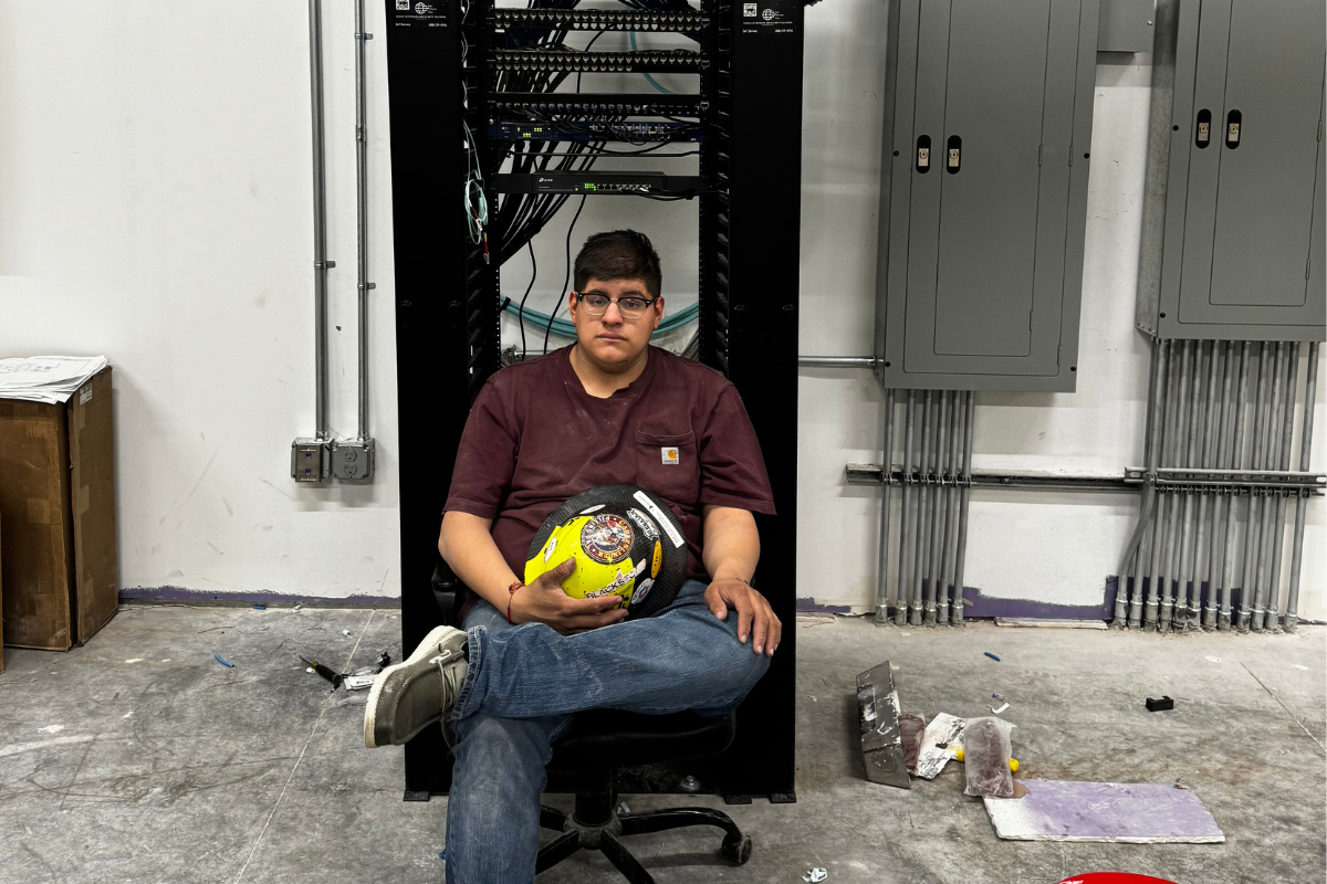 Rick Aguilera sits with a hardhat in front of a piece of computer equipment.