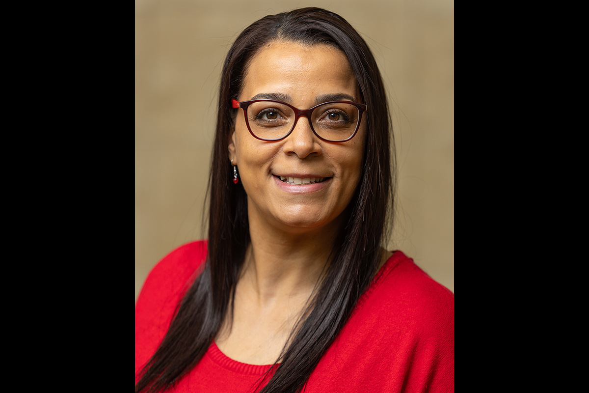 A woman with straight dark hair, wearing red glasses and a red sweater, smiling at the camera against a neutral background."