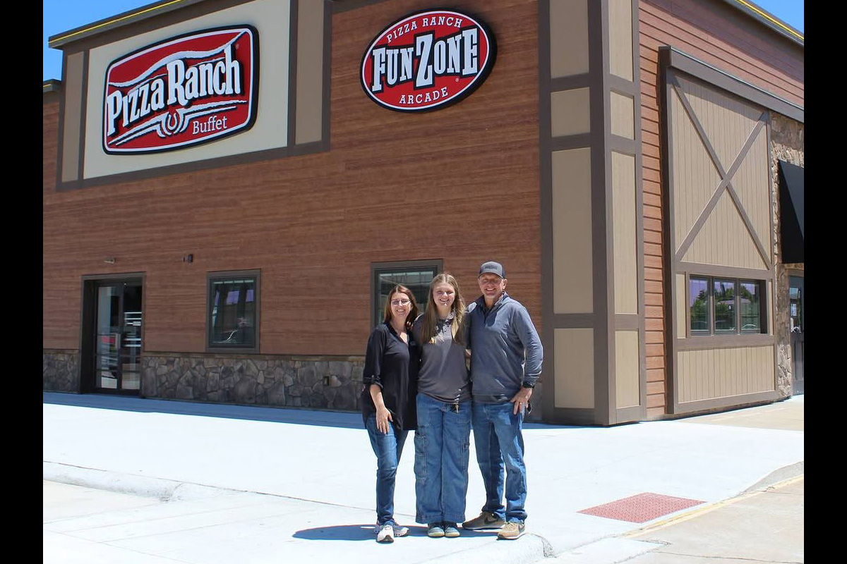 Three people stand smiling outside a Pizza Ranch restaurant with a ‘Pizza Ranch Buffet’ sign and a ‘FunZone Arcade’ sign on the building, under a clear blue sky.