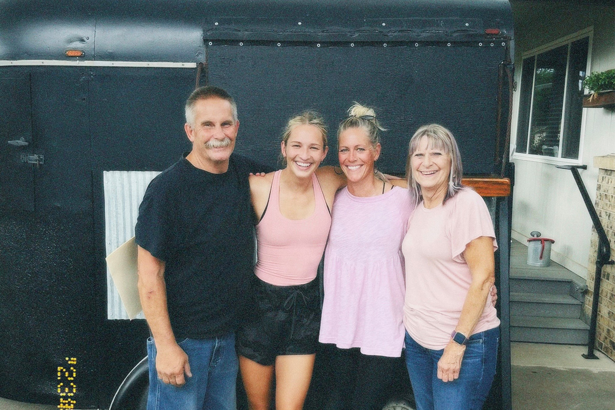 Four people stand arm in arm and smile together in front of The Wandering Lilac mobile food trailer.