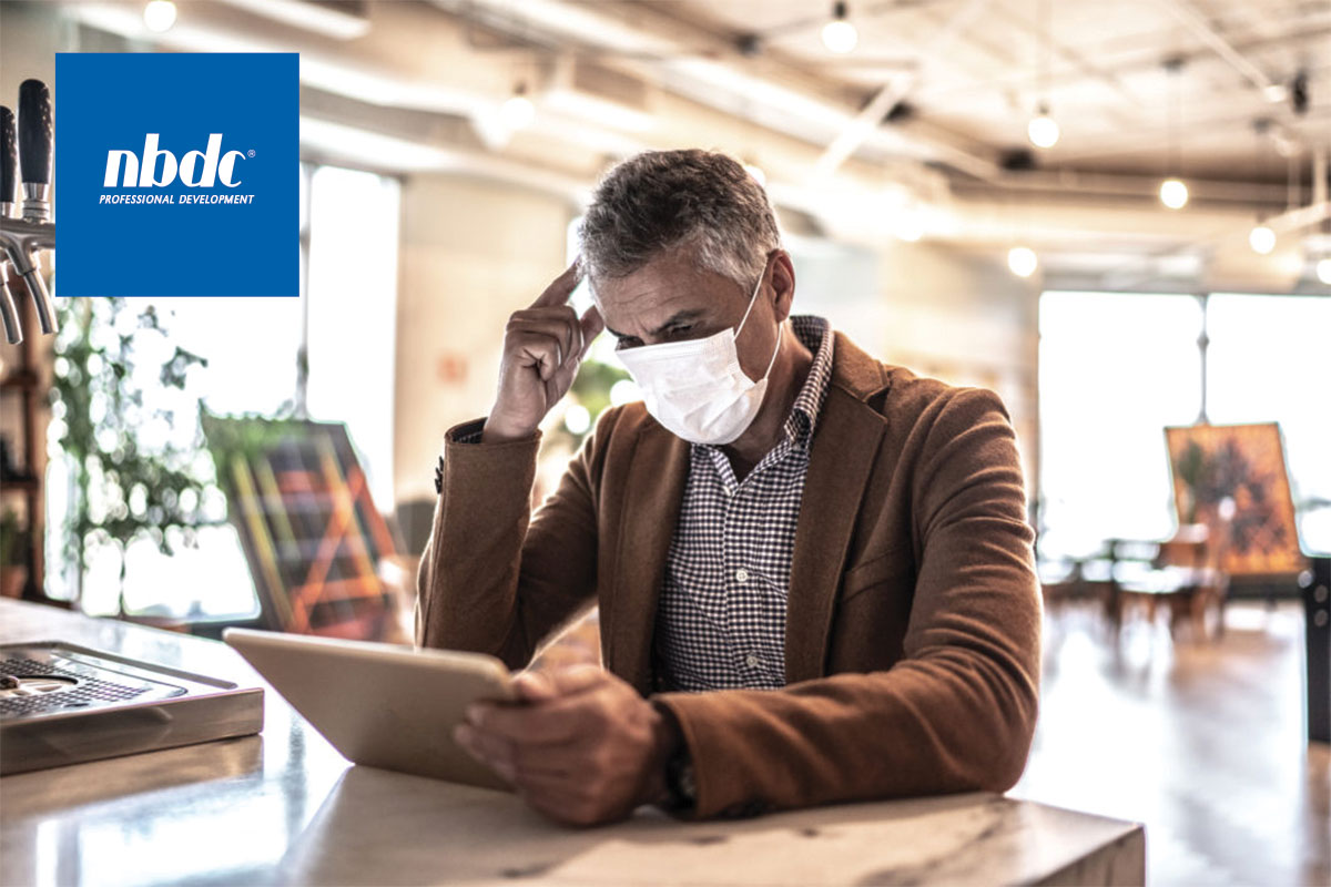 Man with face mask sitting looking at tablet concerned