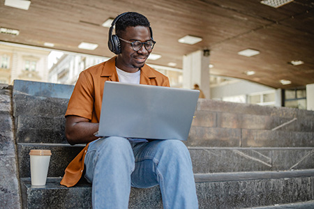 young man wearing headphones and smiling and looking at laptop