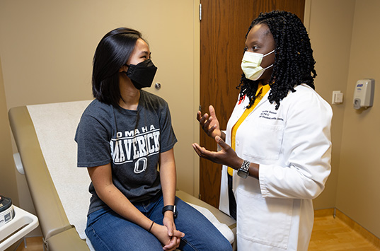 a physician talks with a young patient who is sitting on an exam table