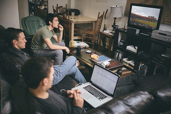 students sit in a room, watching baseball on tv and eating snacks.