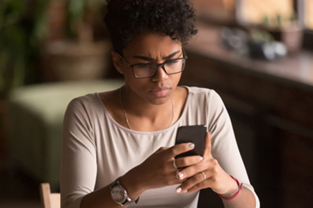 a young woman in glasses looks at her phone as she sits at a table