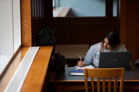 a young woman sits at a library table and studies