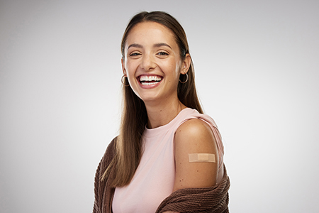 A smiling young woman with her arm exposed showing a bandaid covering her flu shot