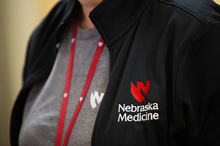A person wearing a black zip up jacket with the Nebraska Medicine logo