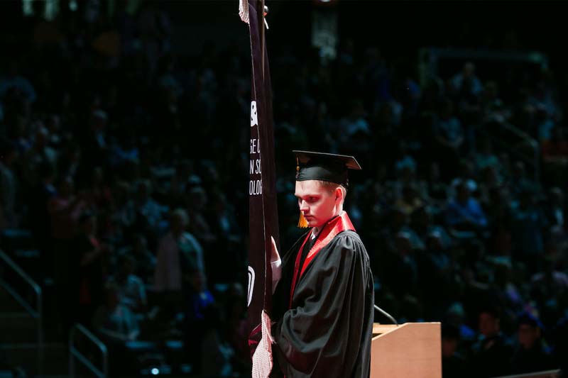John Patrick Nicholson carries the College of Information Science and Technology Banner curing UNO's commencement ceremonies