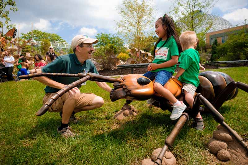 Two children ride a giant plastic ant as a play facilitator helps teach them about the insect