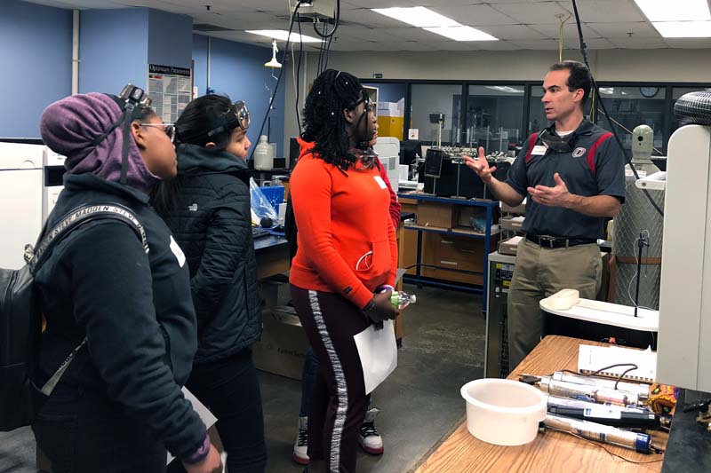 Three students visit with UNO instructor Dana Richter-Egger at one of UNO's chemistry labs