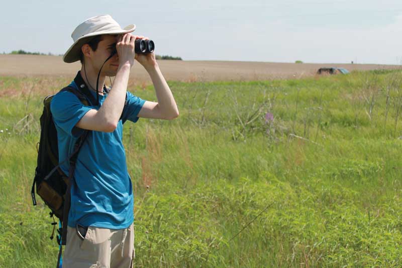 UNO alumnus Conor Gearin looking for birds in a Nebraska field