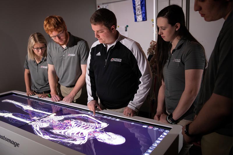 A UNO instructor stands with students as they work on a new Anatomage Table obtained by UNO