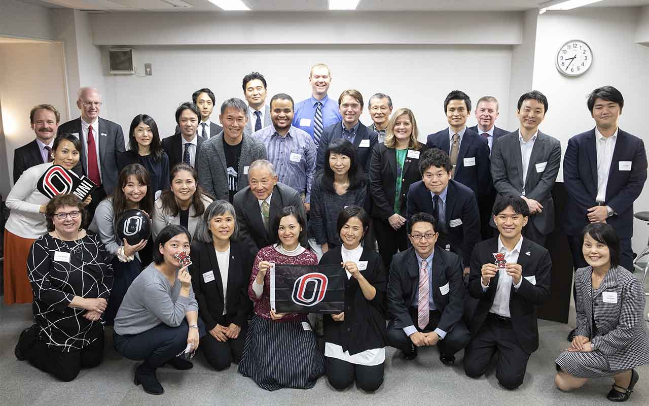 UNO Chancellor Jeffrey P. Gold M.D. and attendees pose with a UNO flag at an alumni event held in Tokyo.