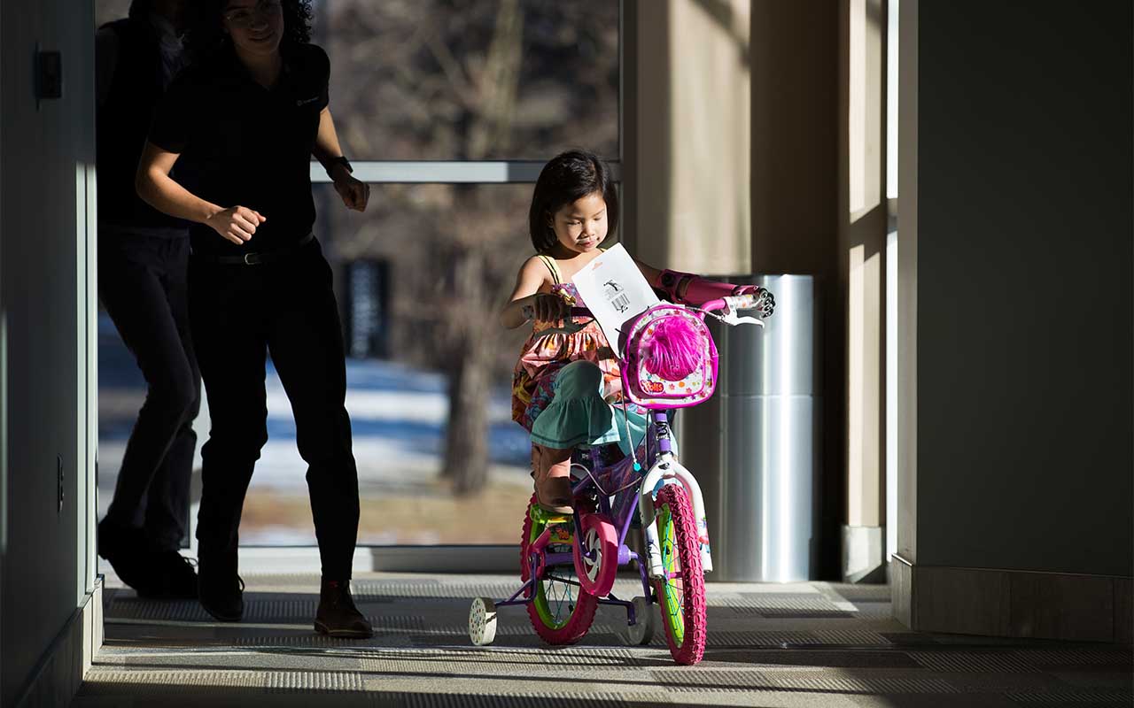 Using her 3D-printed prosthesis, Rue is able to hold onto both handlebars and ride her bike through the hallways of UNO's Biomechanics Research Building.