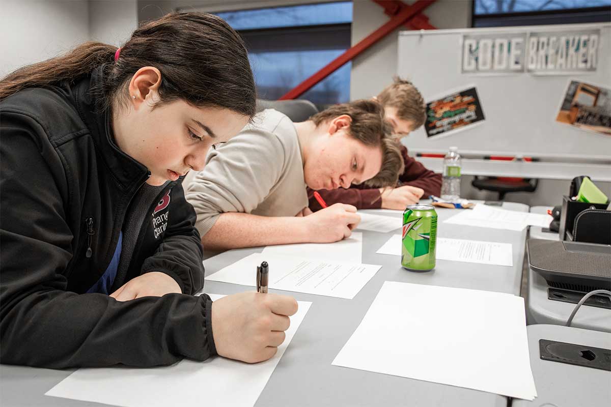 Three students work to decrypt a code using a key as a guide during the Code Breaker activity.