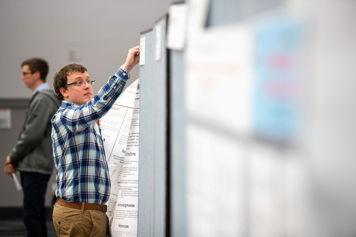 A student places his poster presentation up for display