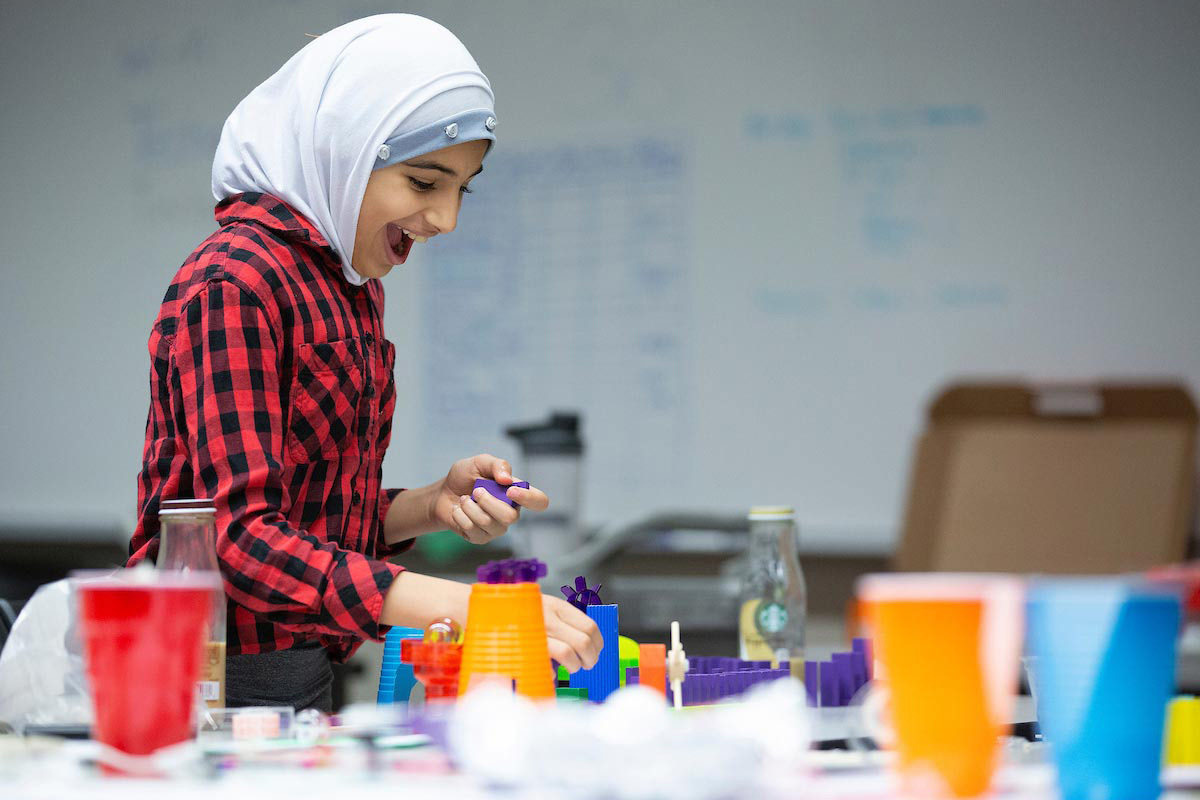 A young girl enjoys sorting through materials to put together a Rube Goldberg device during a UNO summer camp