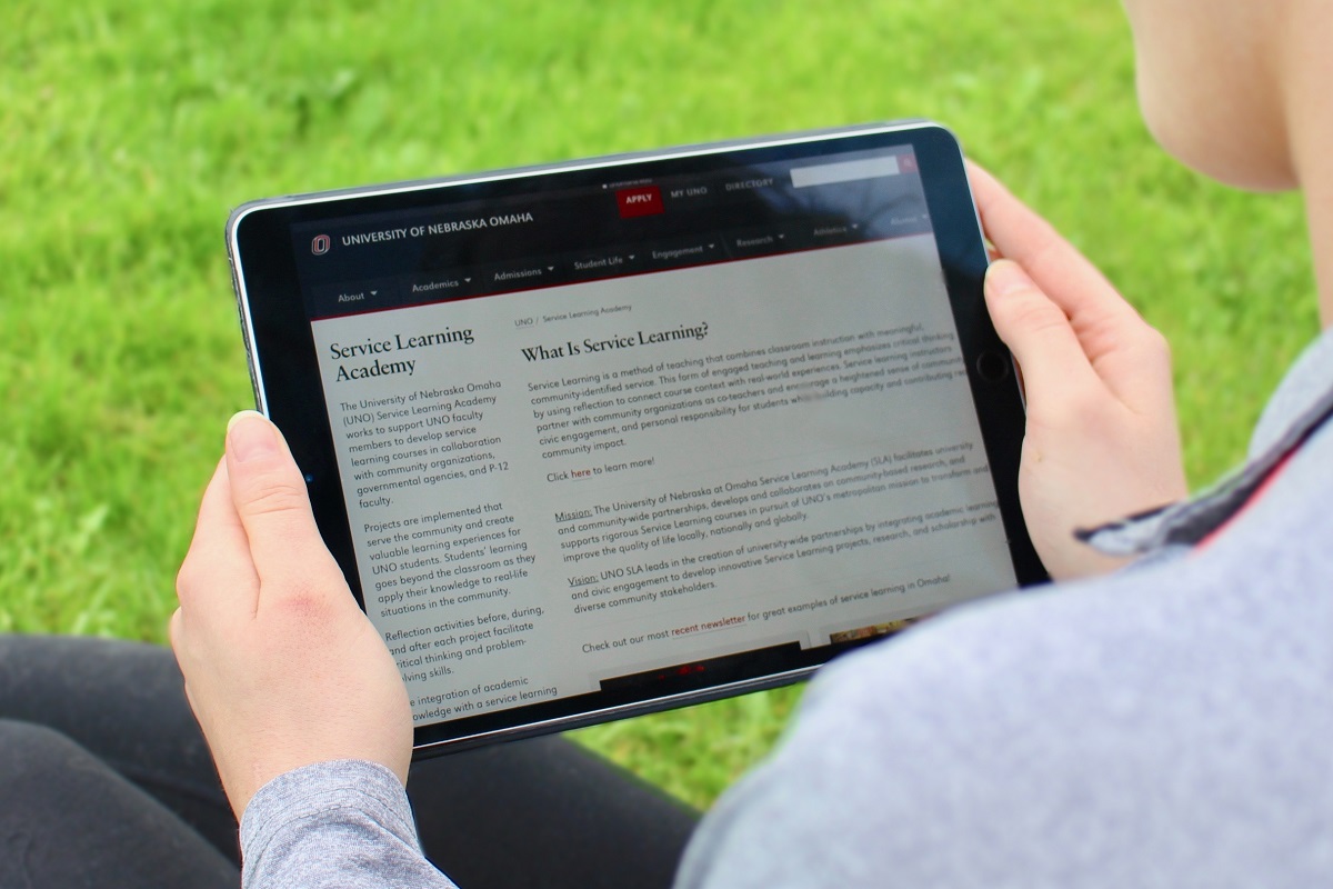 A student holds a tablet pulled to the Service Learning Academy website.