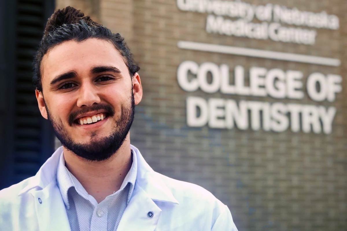 A photo of Elias Witte in a white lab coat outside the College of Dentistry building on UNMC's campus.