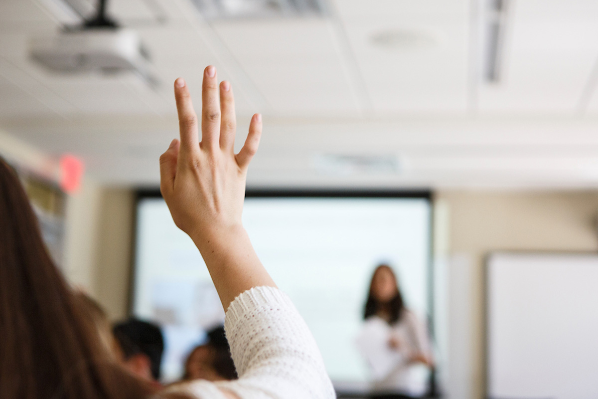 student in classroom with hand raised