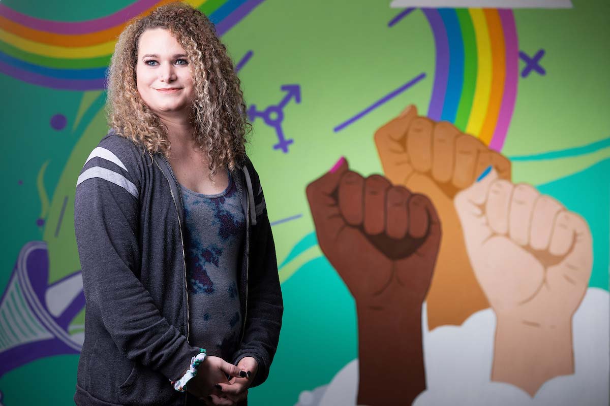 A photo of UNO student Ally Nelson by a mural in the Milo Bail Student Center