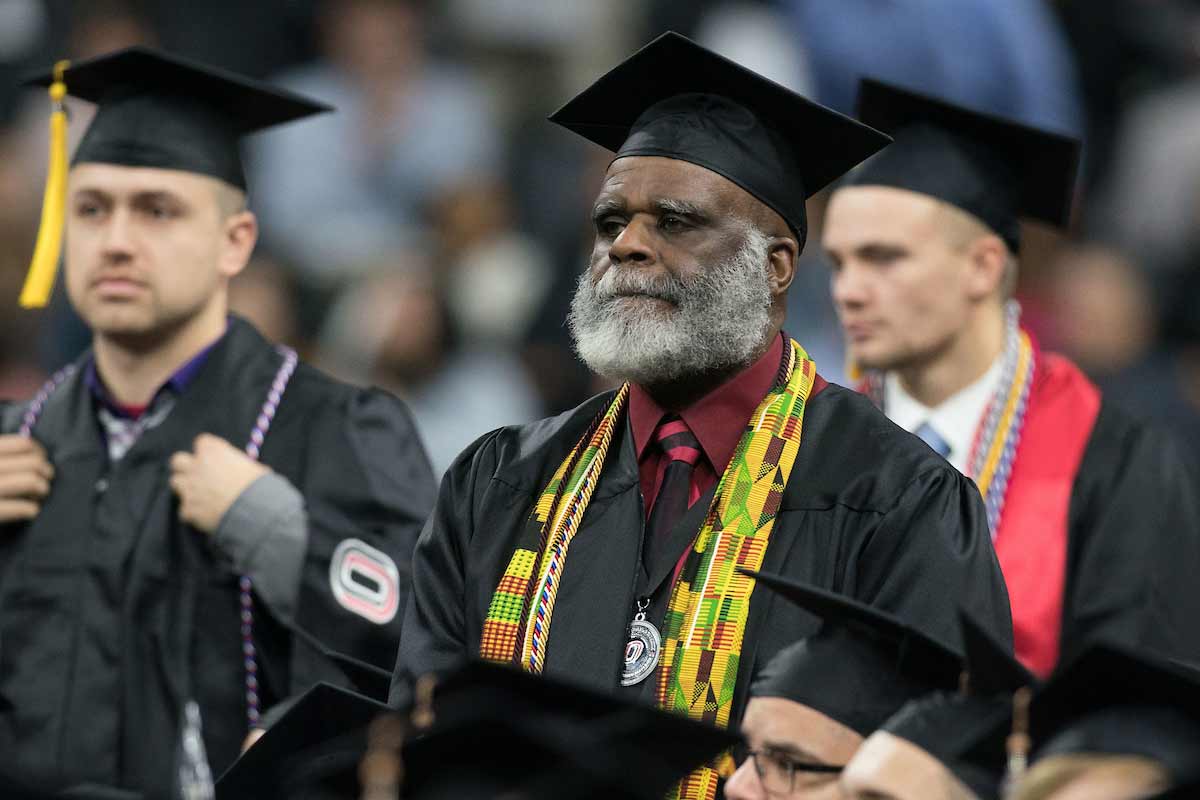 An older student stands up during UNO's 2019 commencement ceremonies.