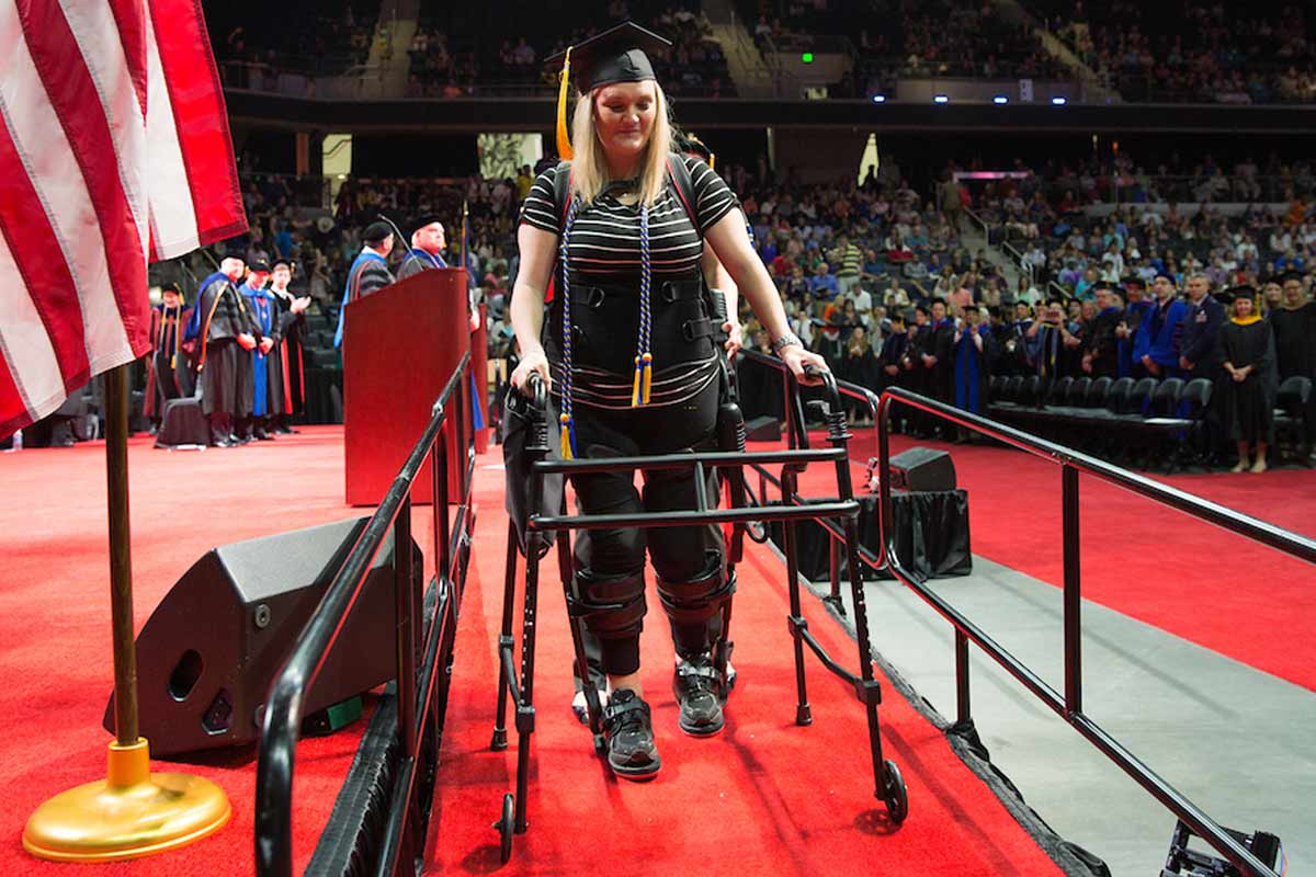 Taryn Schaaf walks across the stage at her graduation with the use of an exoskeleton provided by QLI.