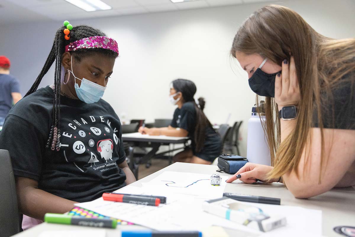 A camper and UNO student work together on robotic programming at UNO's Techademy