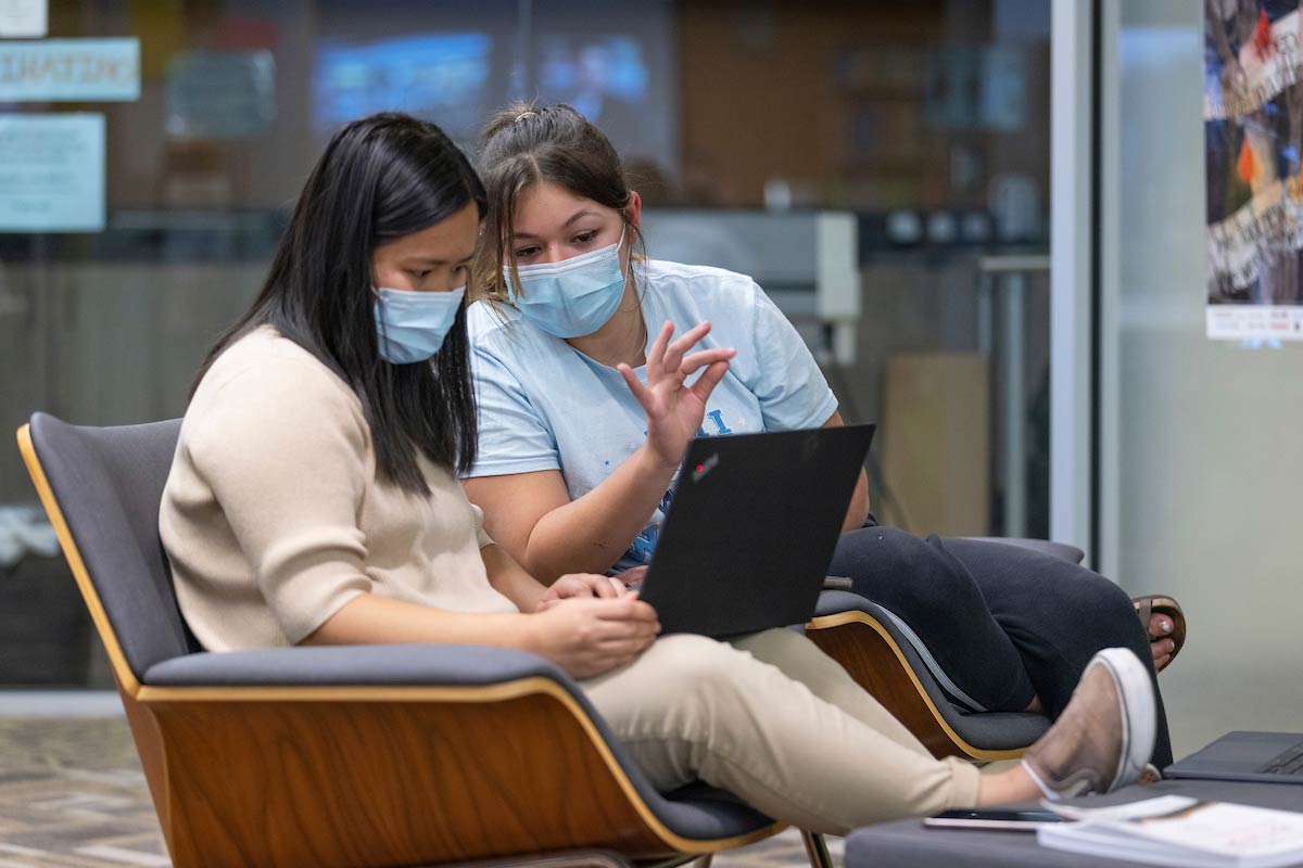 Two students sit with a computer in front of them.