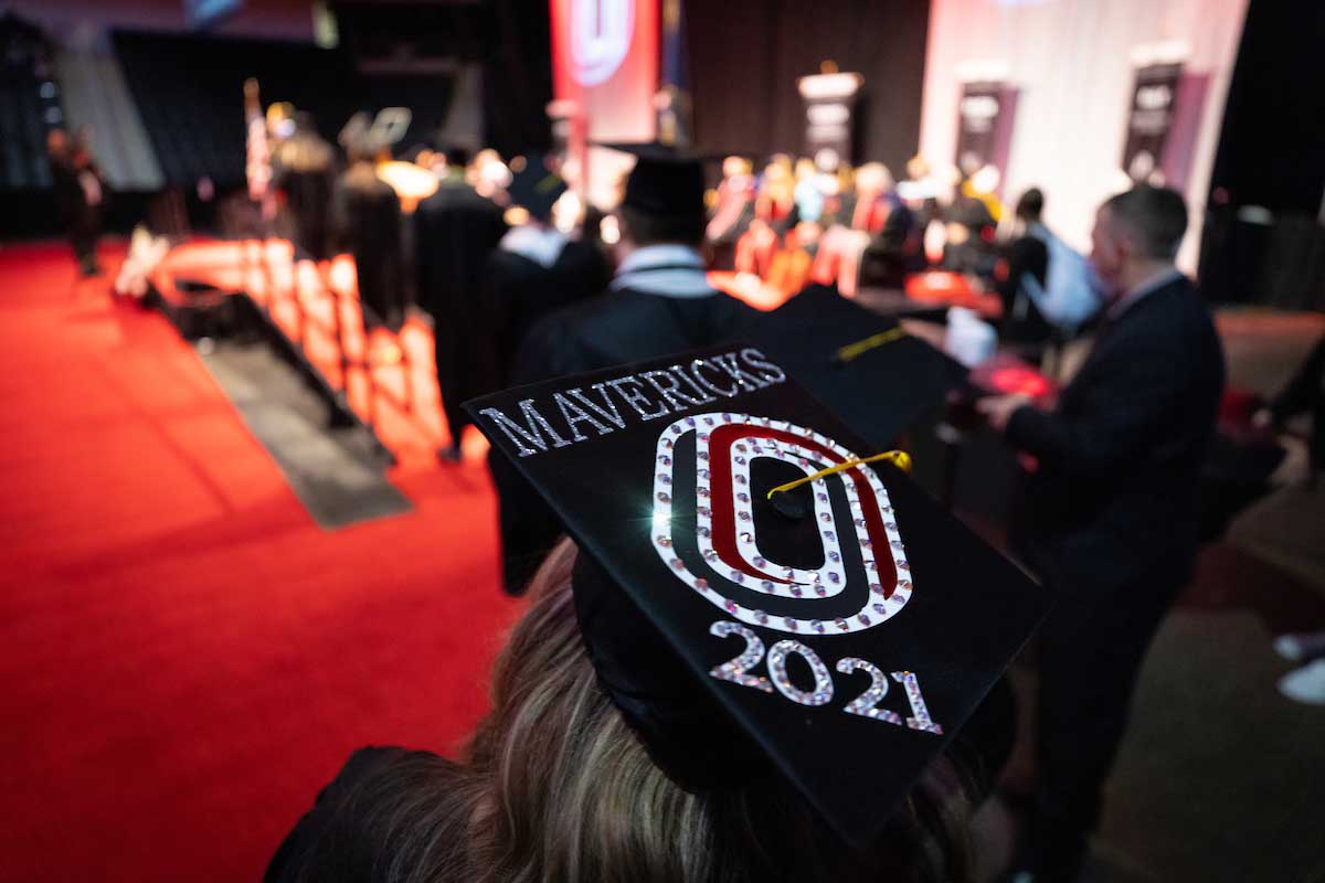 A student prepares to walk across the stage with a "UNO" designed cap.