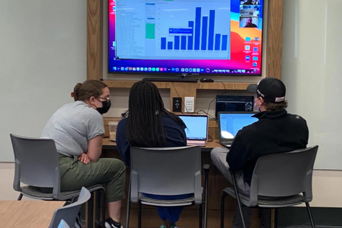 Students sit in front of a monitor. 