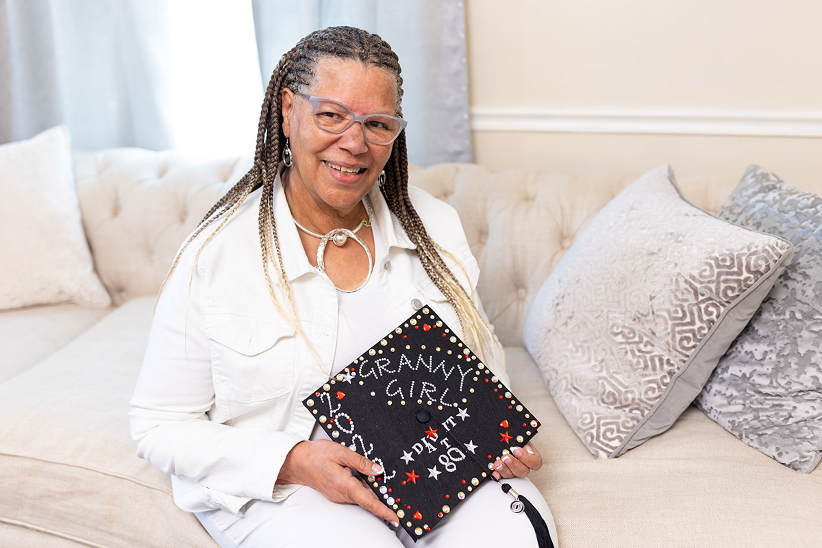 Madeline Adams holding her decorated graduation cap decorated in bedazzled words read “Did It At 80” and “Granny Girl."