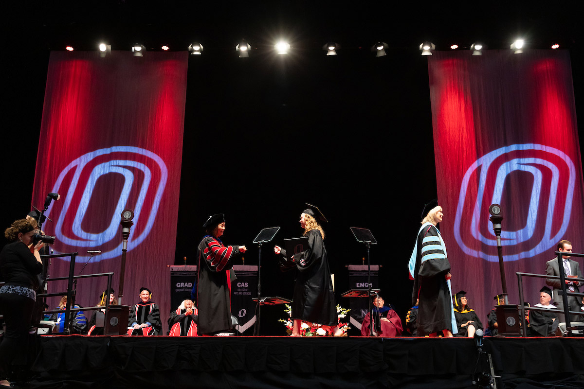 UNO Chancellor Joanne Li, Ph.D, CFA, (left) gives a graduating student a fist bump on stage