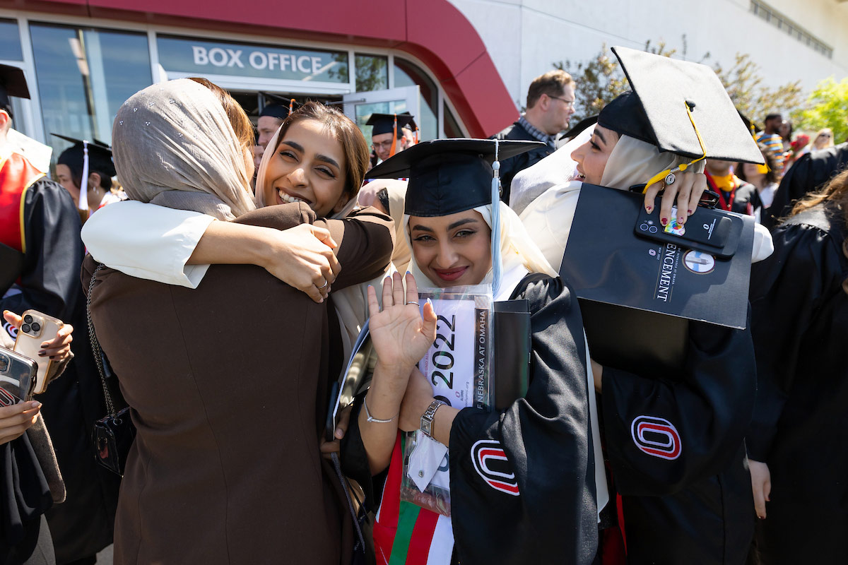 New alumni celebrate outside of Baxter Arena, one waving at the camera while holding her diploma and license plate.