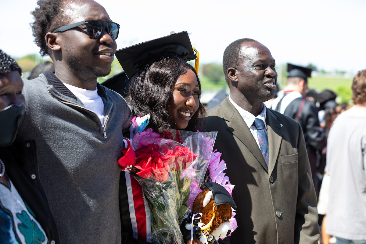 Friends and family celebrate with a graduate outside of Baxter Arena, posing for a photo.