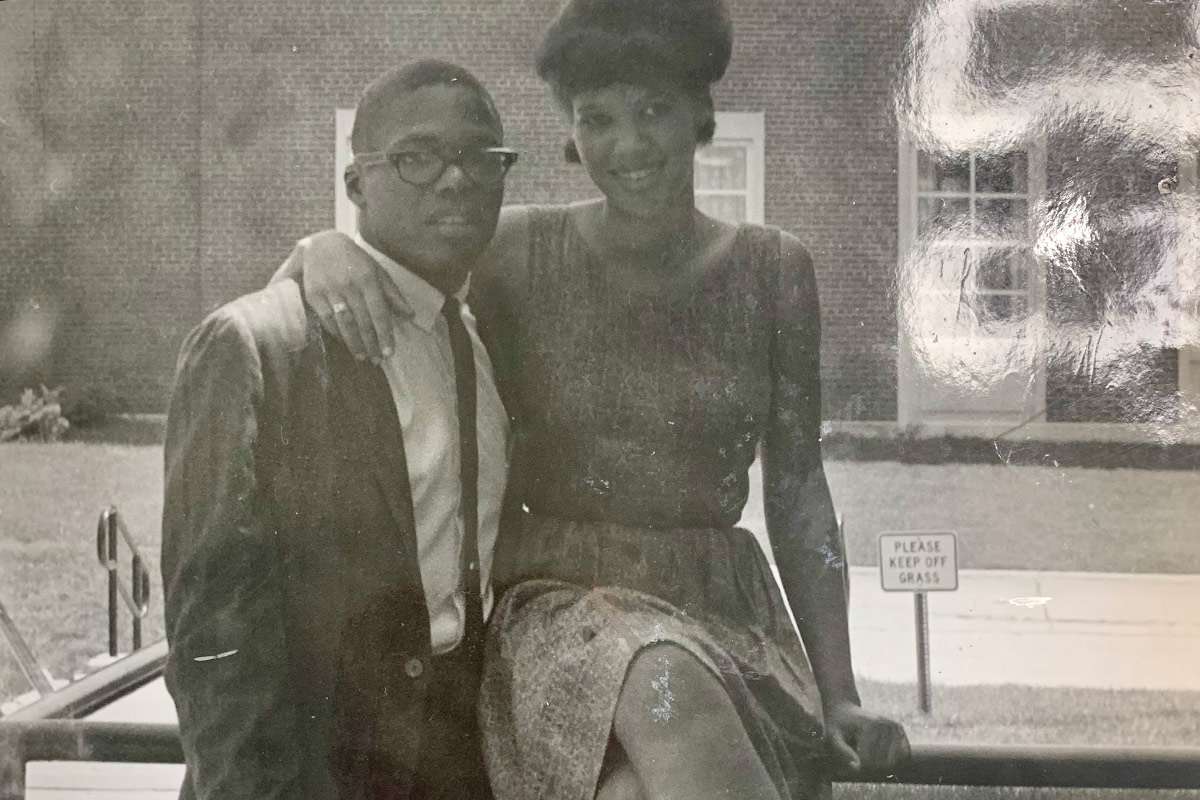 Madeline Adams sitting on a railing on campus, posed next to her husband.