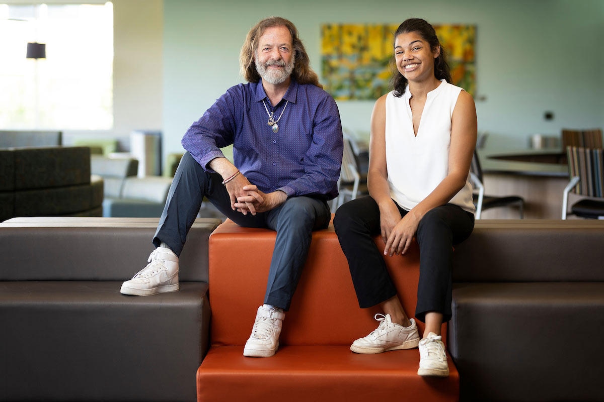 AT Miller and Tori Sims sit on a gray and orange tiered couch in the lobby of the Weitz CEC