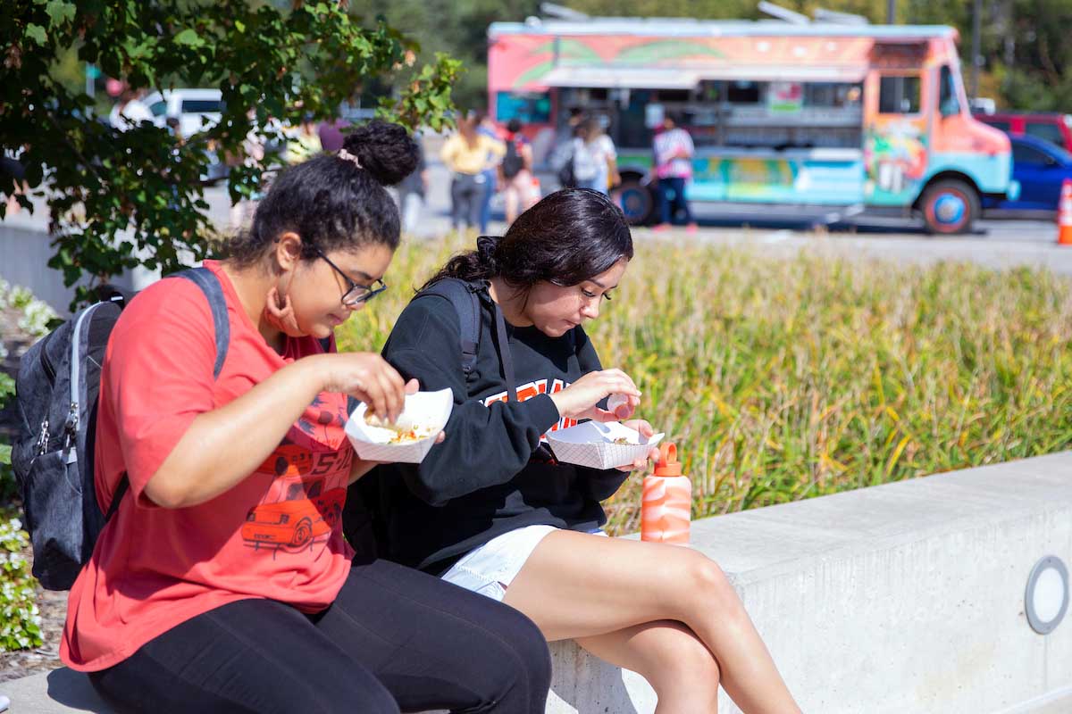 Two students sit by the Henningson Memorial Plaza after getting food from a local food truck during a campus event.