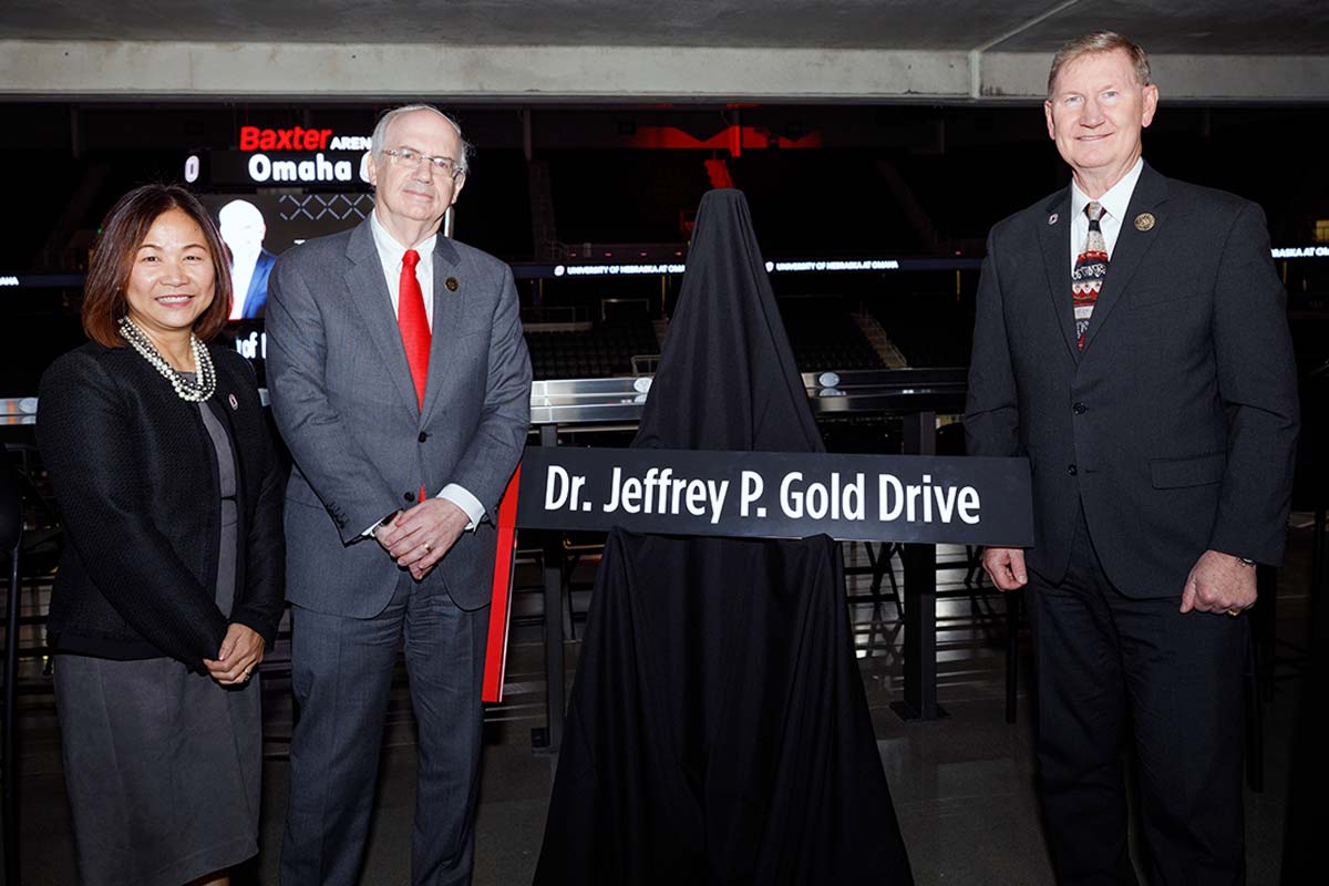 Joanne Li, Jeffrey Gold, and Ted Carter stand for a photo at Baxter Arena with a sign reading "Dr. Jeffrey P. Gold Drive" in the center.