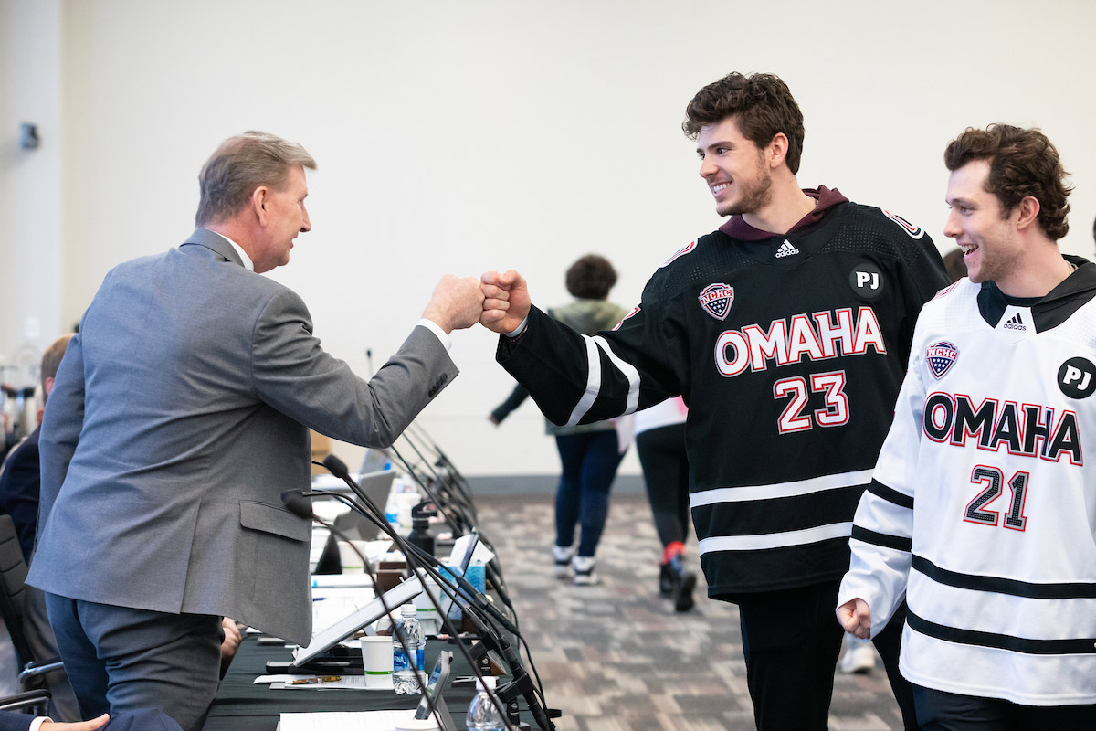 Omaha Hockey players Victor Mancini (#23) and Tyler Rollwagen (#21) offered University of Nebraska System (NU) President Ted Carter a fist bump.