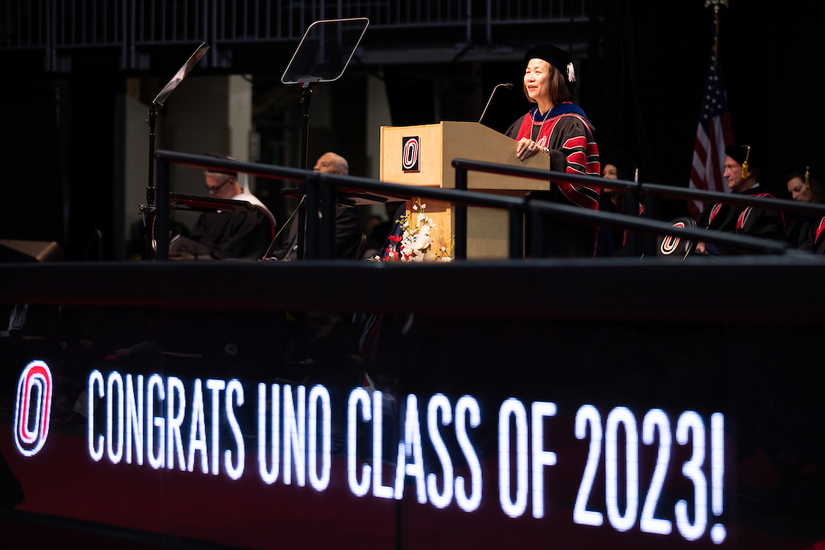 Chancellor Joanne Li, Ph.D., CFA, speaks to the grads-to-be with a "Congrats UNO Class of 2023" sign nearby